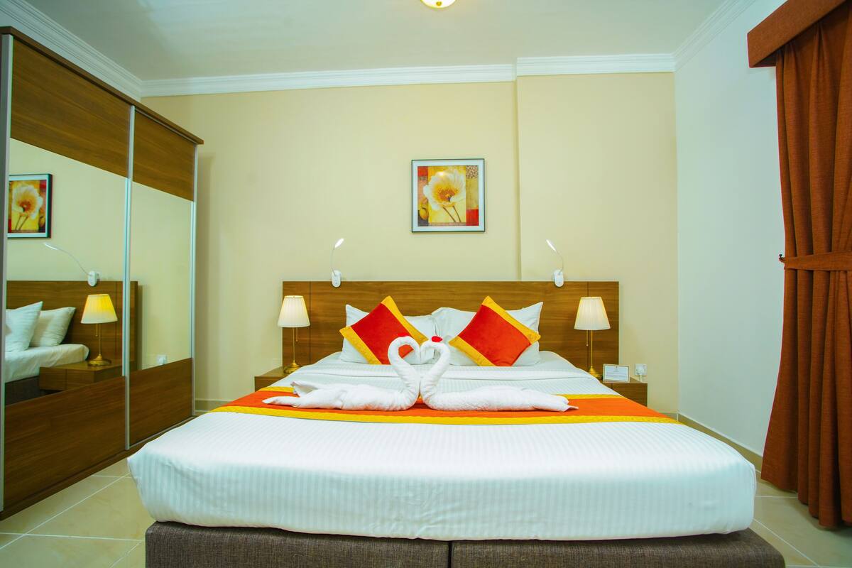 A neatly made bed with a heart-shaped towel arrangement, a mirror, and a painting on the wall.