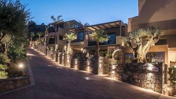 Un hotel de varios pisos con un camino pavimentado, muros de piedra y palmeras.