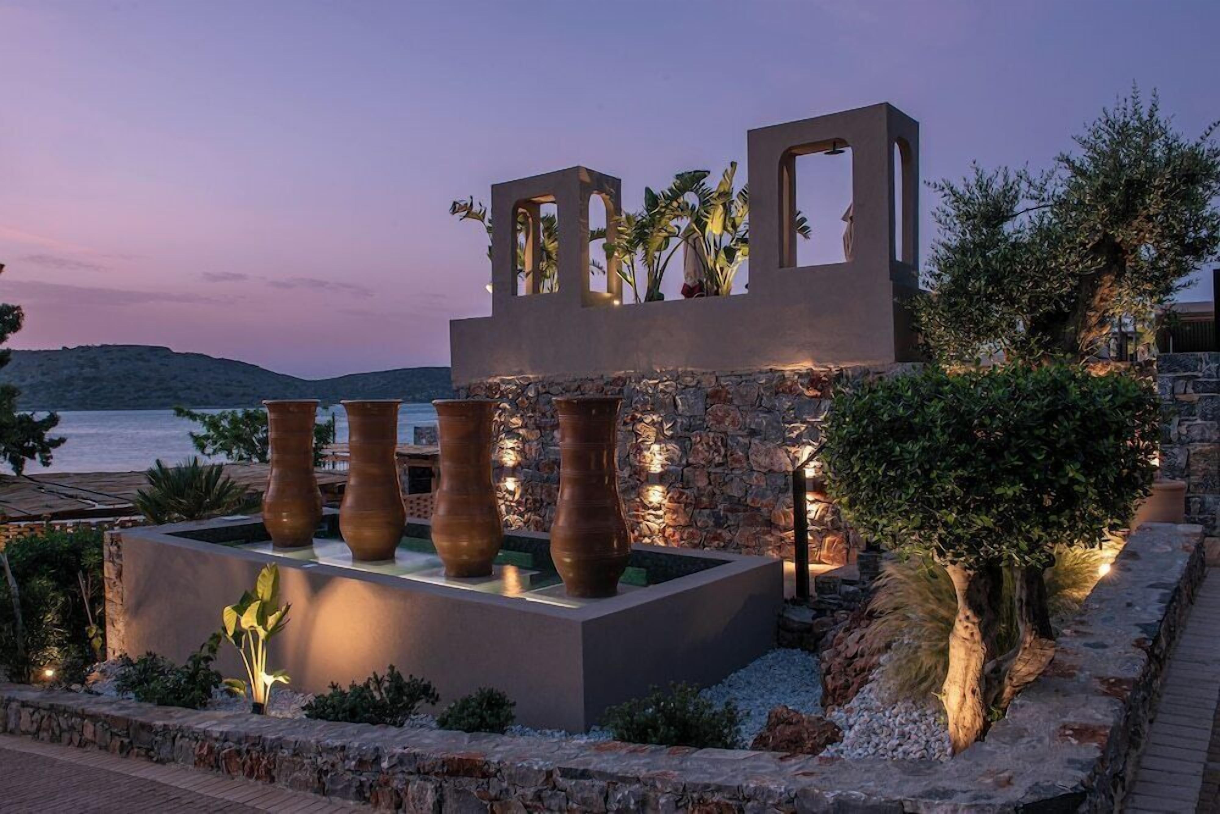 Una estructura moderna al aire libre con muros de piedra y grandes jarrones, con vistas a un cuerpo de agua.