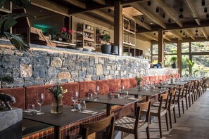 Um restaurante com paredes de pedra, vigas de madeira e uma longa mesa de jantar com cadeiras.
