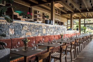 A restaurant with stone walls, wooden beams, and a long dining table with chairs.
