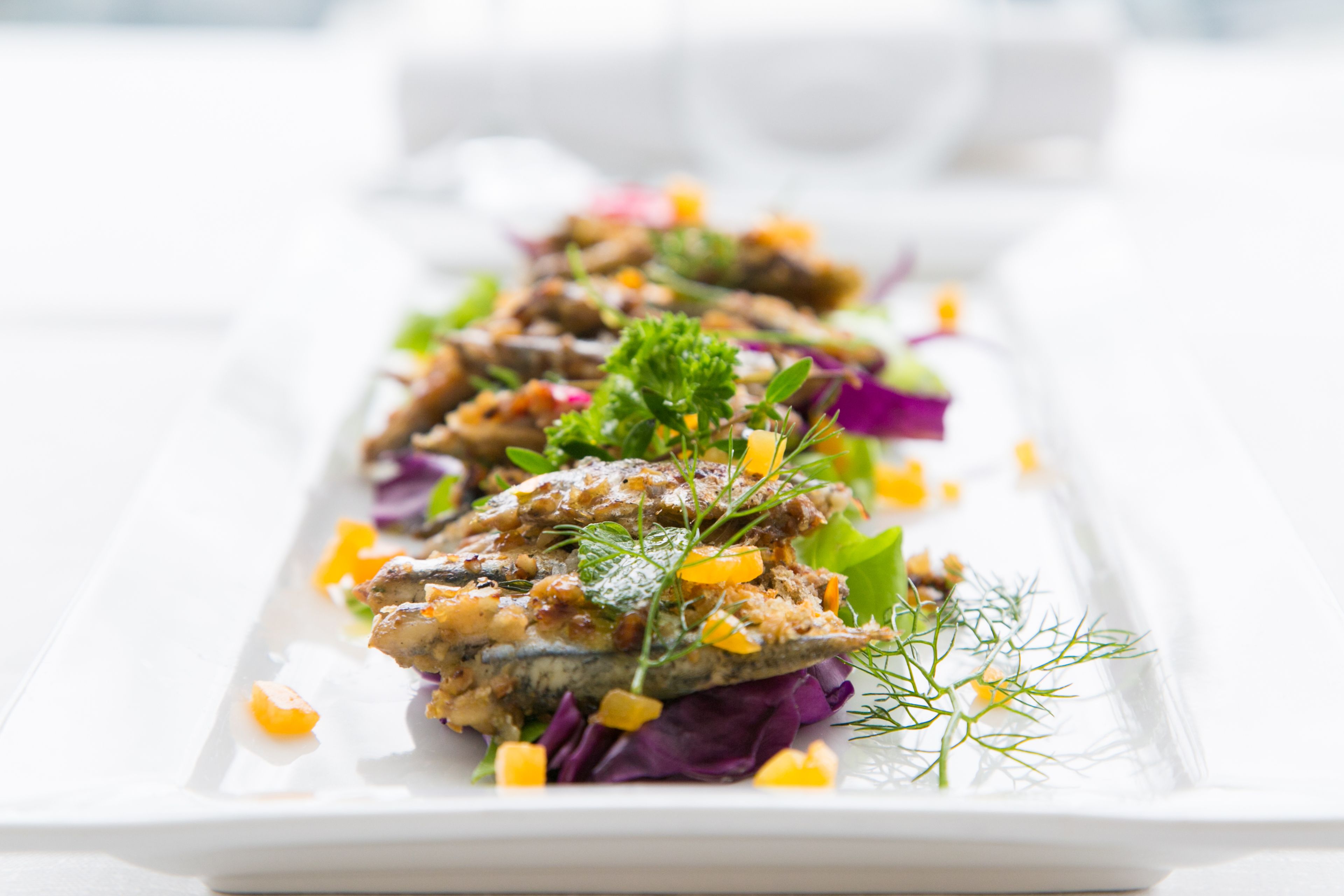 Un plato rectangular blanco con un plato de mariscos, adornado con hierbas y verduras.