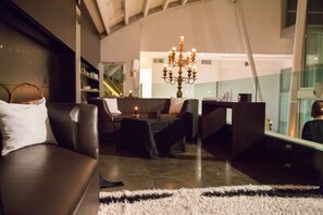 A modern interior with a dark leather sofa, a chandelier, and a view of a cityscape through a large window.