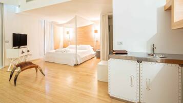 Una camera d'albergo moderna con un ampio letto, una televisione, una sedia di legno particolare e un angolo cottura.