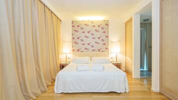 Habitación de hotel con una cama grande, dos lámparas de noche, un papel tapiz estampado con motivos florales y suelo de madera.