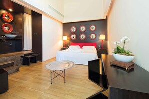 A modern hotel room with a bed, bedside lamps, a small table, and a bowl of flowers.