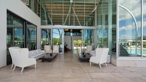 A modern outdoor lounge area with white sofas and tables, large glass windows, and a view of a pool. - Riviera Golf Resort (San Giovanni In Marignano)