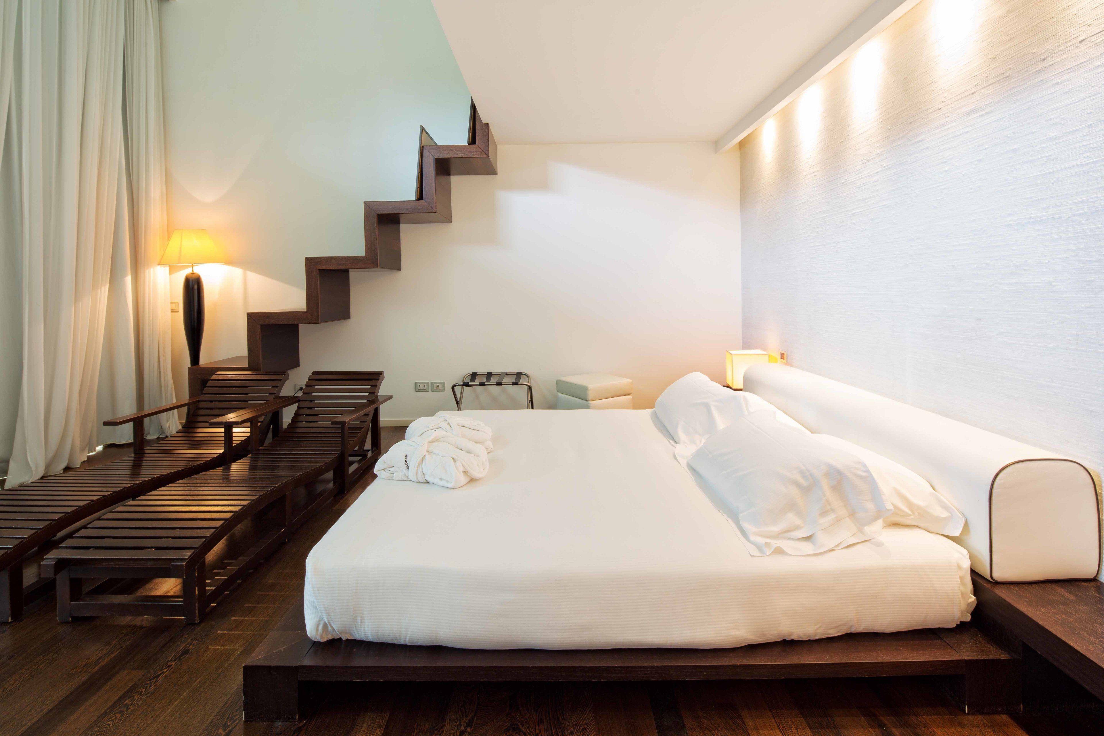 A modern hotel room with a large bed, wooden staircase, and a view of the outdoors.
