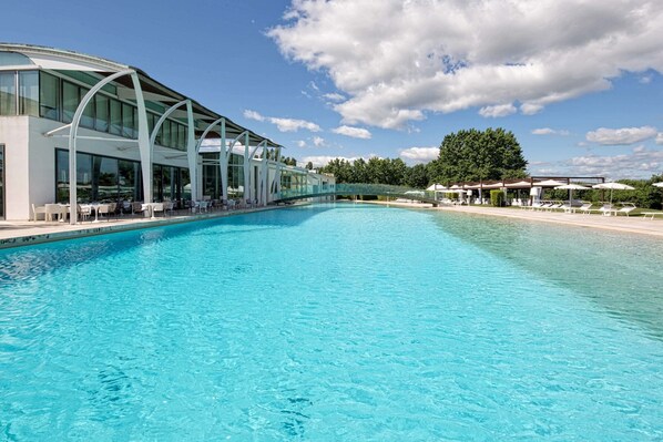 A modern hotel with a large pool, outdoor seating, and a glass-enclosed structure.