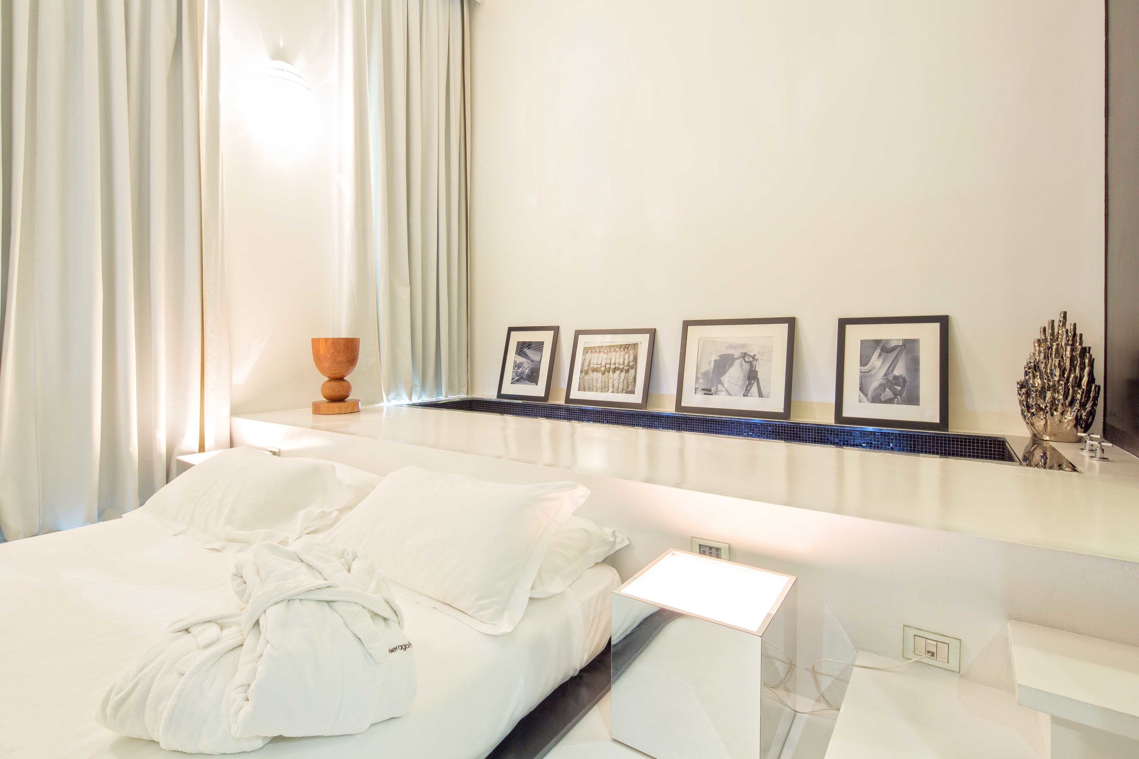 A hotel room with a bed, a nightstand, a mirror, and a wall with framed pictures.