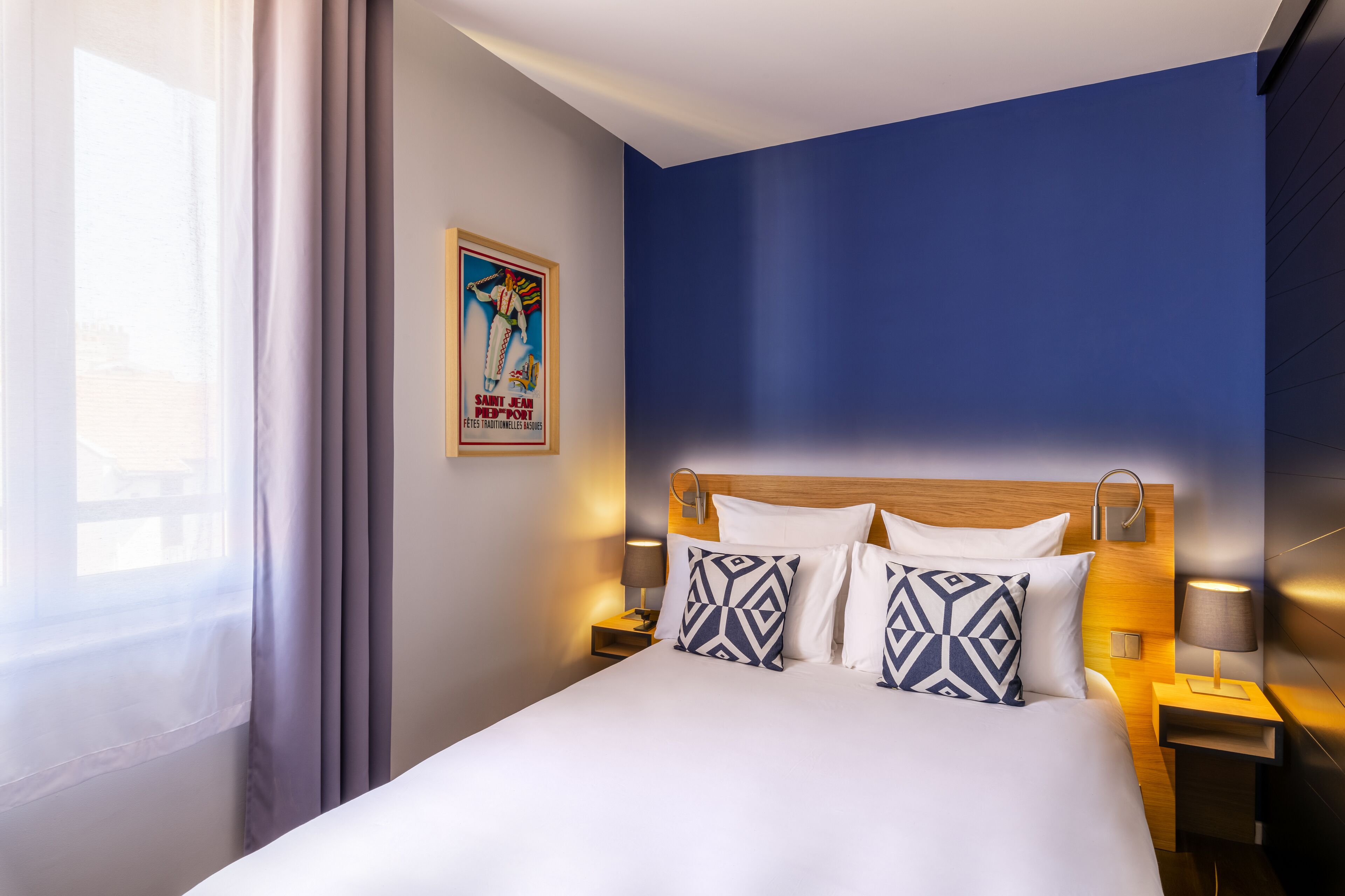Habitación de hotel con una cama grande, dos mesitas de noche con lámparas, un cartel en la pared y una ventana con cortinas.