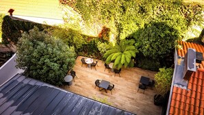 An outdoor patio area with a wooden floor, several tables and chairs, and lush greenery. - Hôtel Villa Koegui Biarritz (Biarritz)
