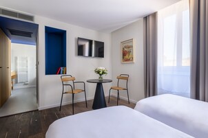 Habitación de hotel con cama, televisión, una mesita con sillas y ventana con cortinas.