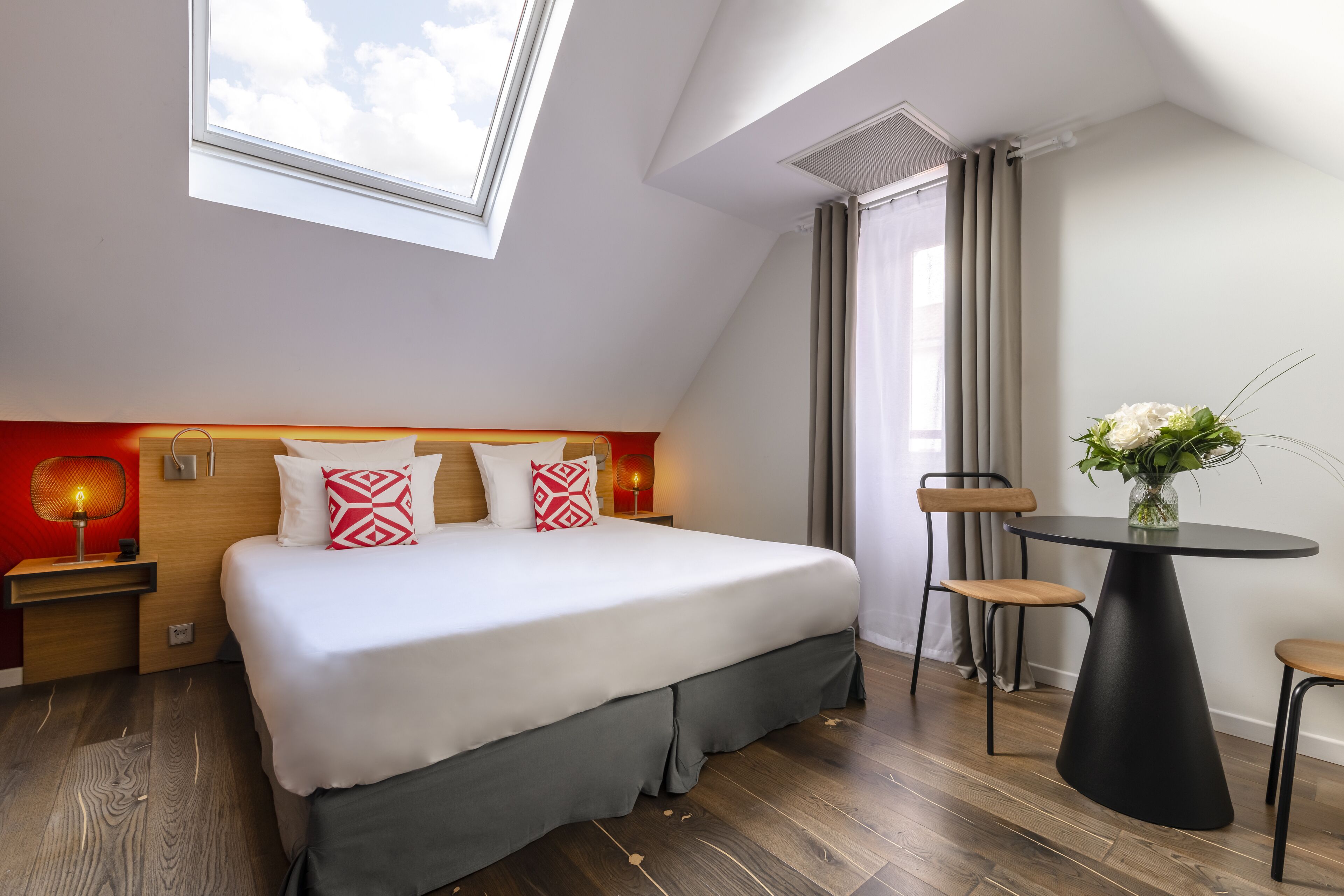 A modern hotel room with a large bed, a desk, and a dining table.