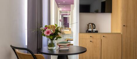A modern room with a round table, a wooden chair, a vase with flowers, and a flat-screen TV mounted on the wall.