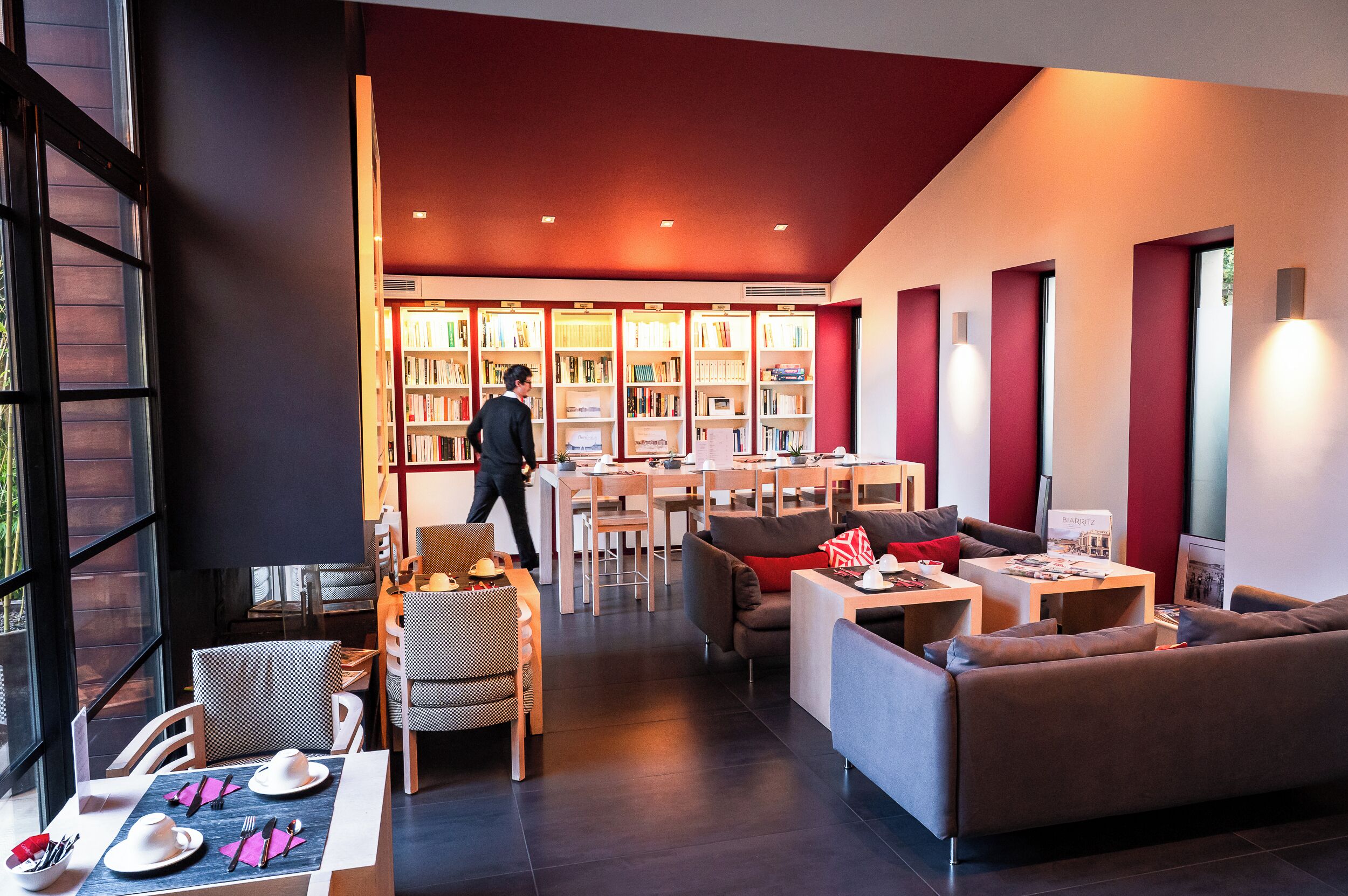 A modern hotel lobby with a dining area, seating, and a large bookshelf.