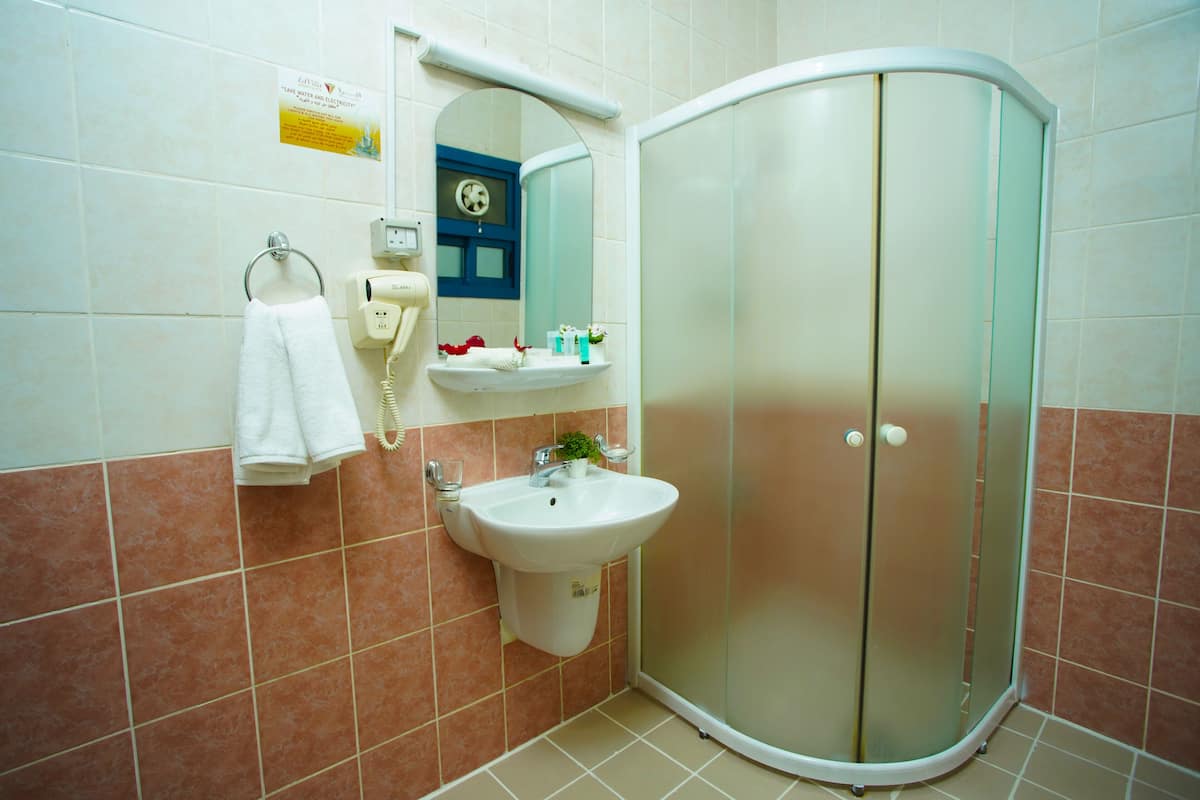 A bathroom with a sink, a mirror, a towel ring, a glass, and a shower enclosure.