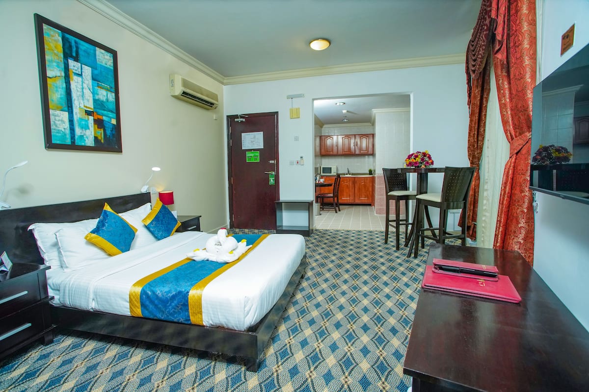A hotel room with a bed, a desk, a chair, a dining area, and a kitchen.