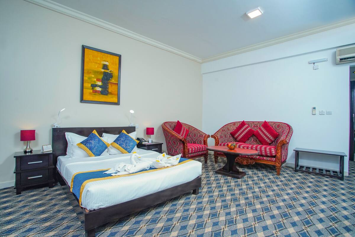 A hotel room with a bed, two armchairs, a small table, and a painting on the wall.