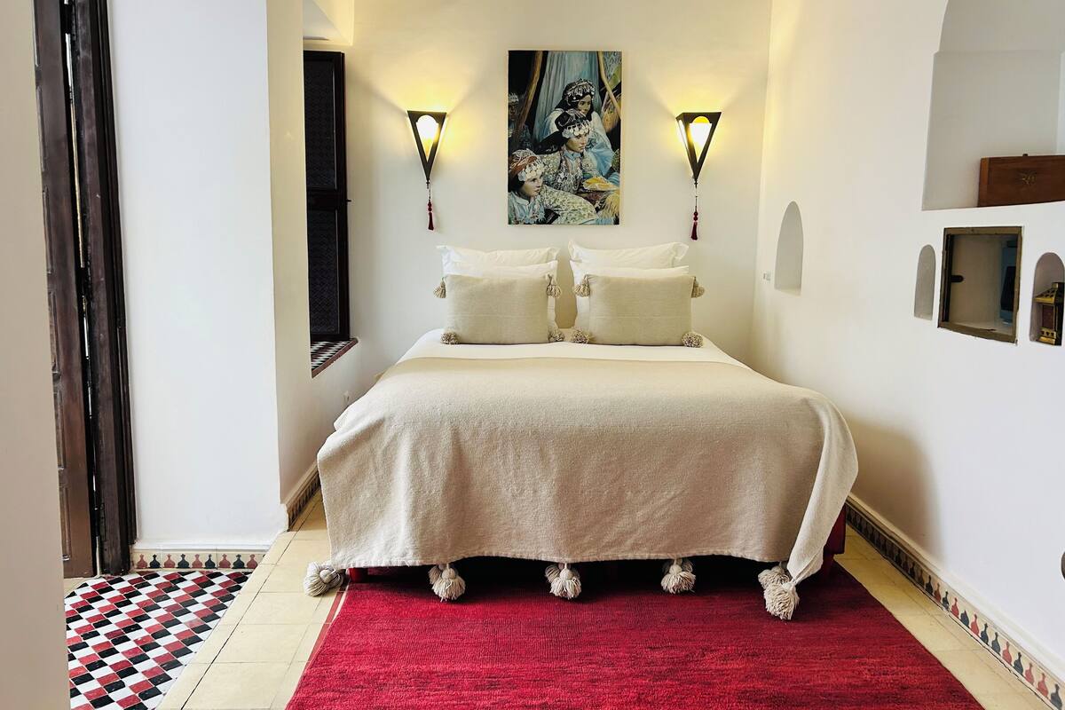 A neatly arranged bedroom with a large bed, two wall-mounted lamps, and a painting above the bed.