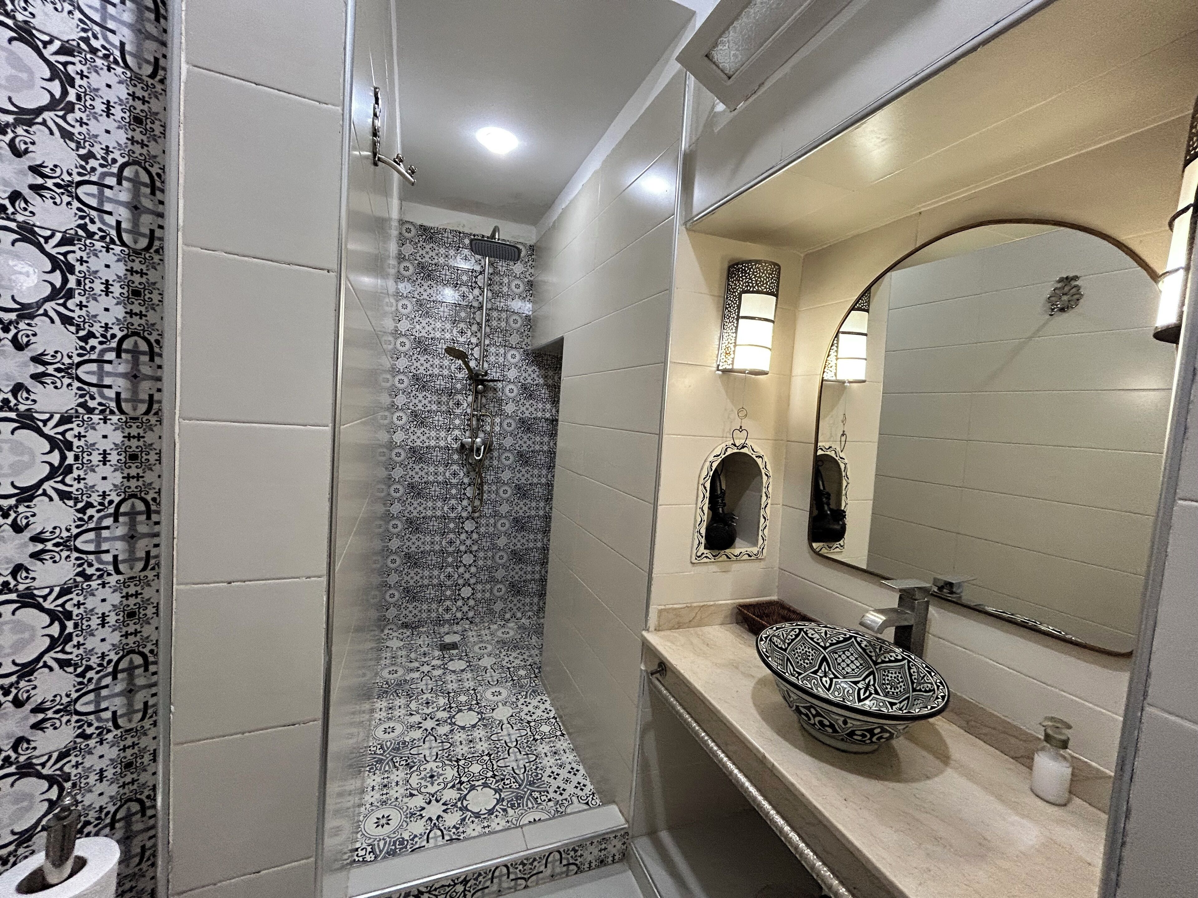 Een badkamer met een douche, een wastafel met een decoratieve kom en een spiegel met verlichting.