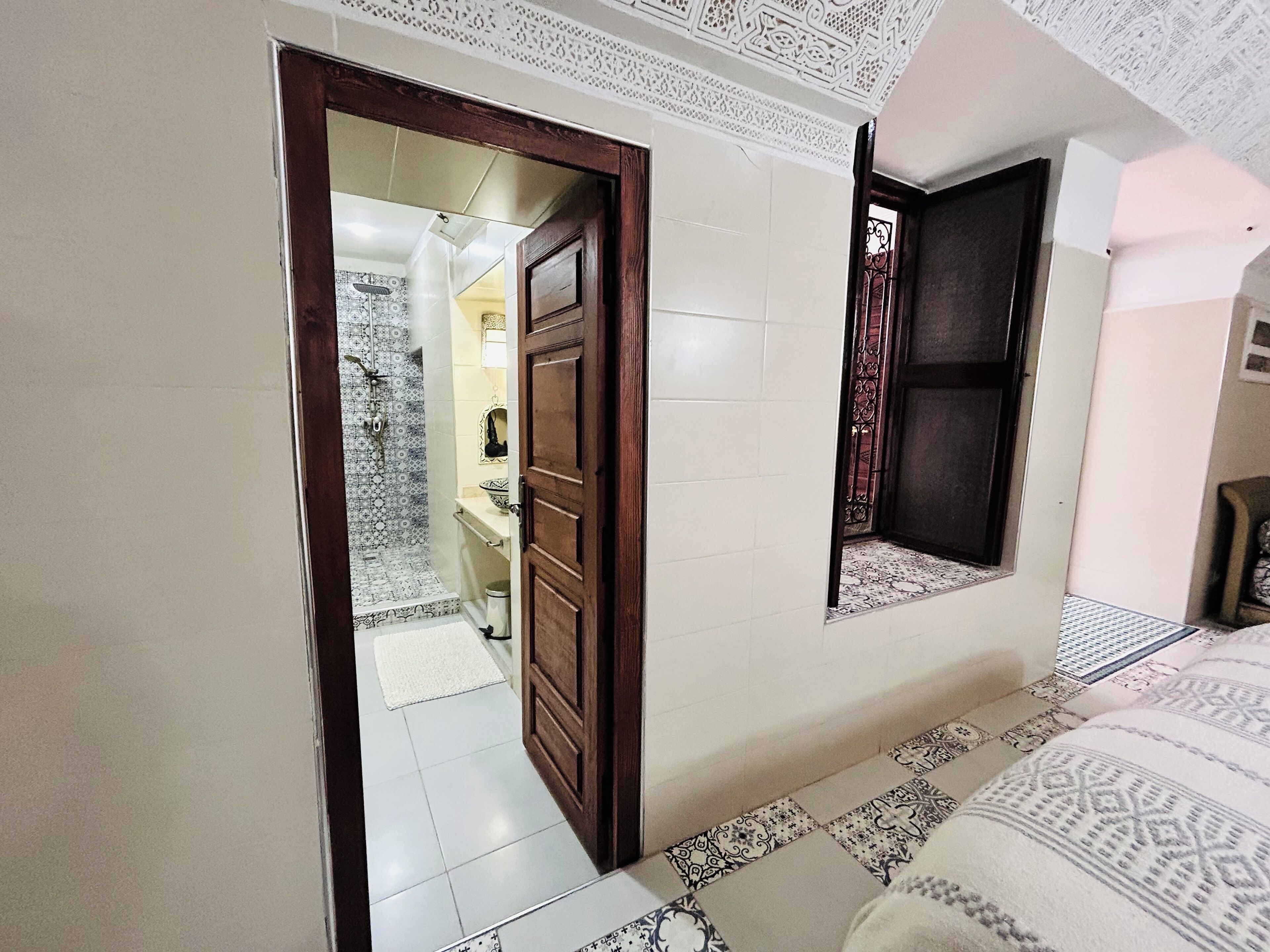 A hallway with a patterned floor, a wooden door, and a small window with a view of a balcony.
