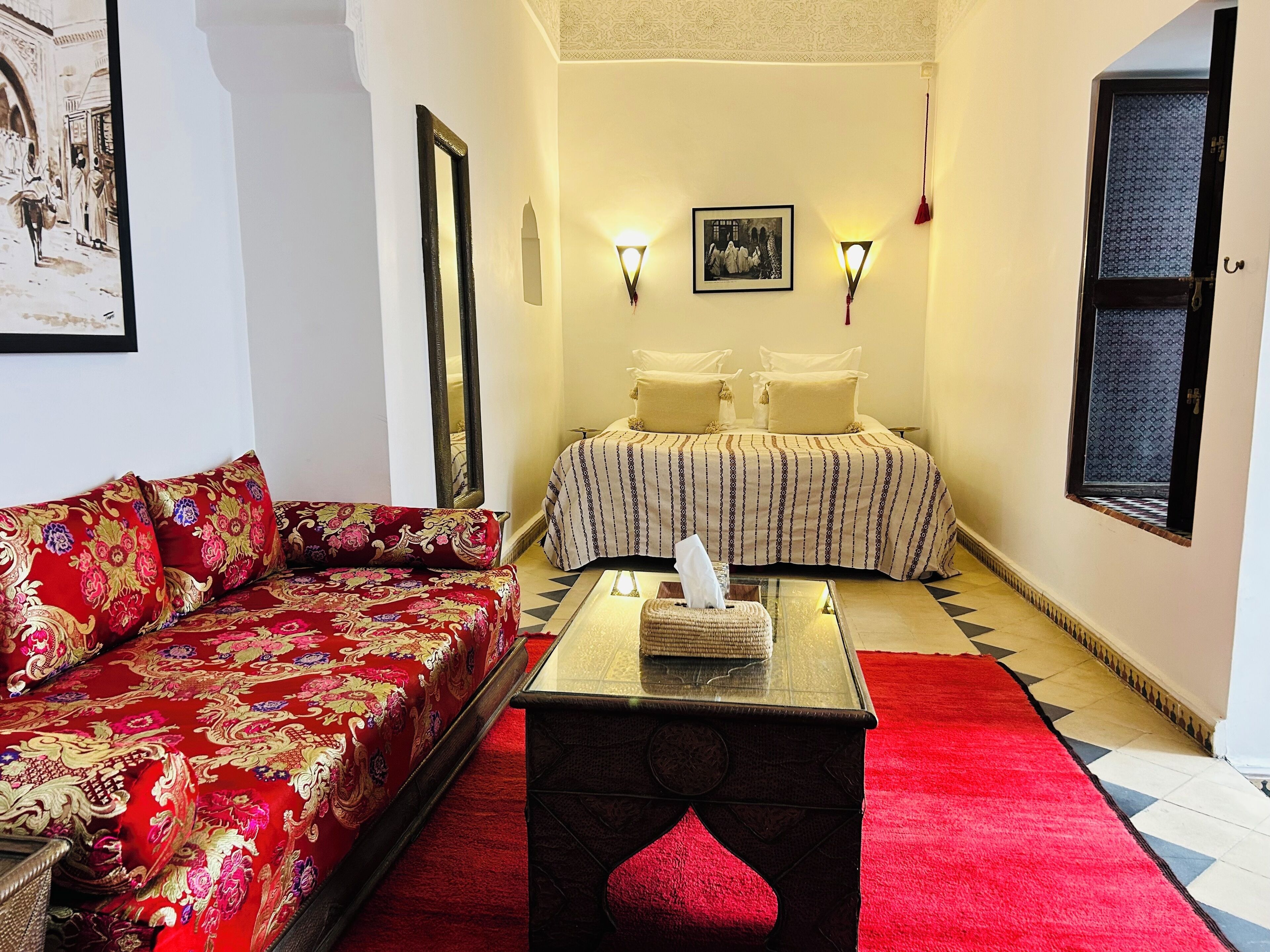 Un pasillo estrecho con un sofá rojo, una cama con ropa de cama a rayas y una pequeña mesa con una caja de pañuelos.