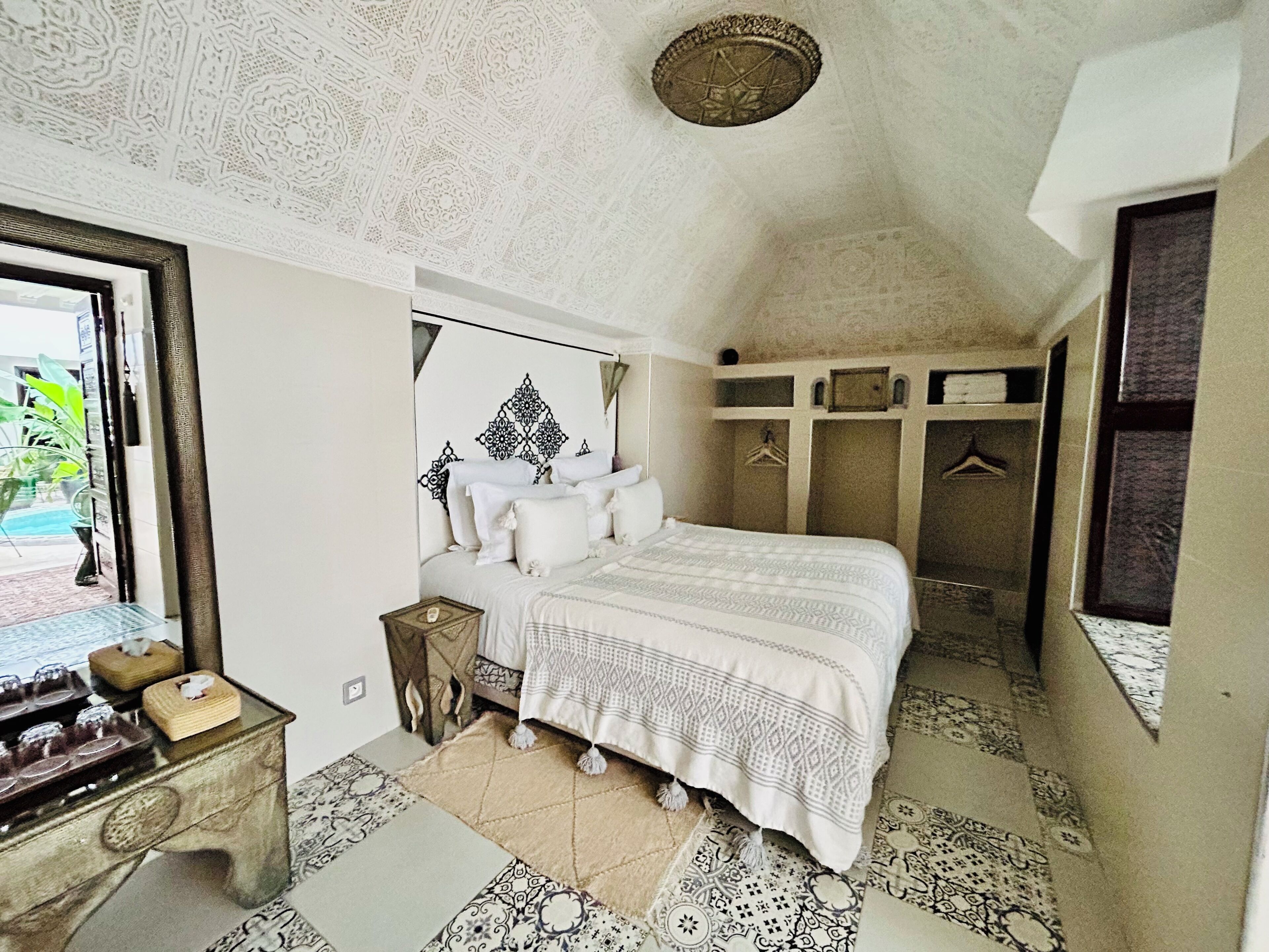 A bedroom with a large bed, a bedside table, a mirror, and a wardrobe.