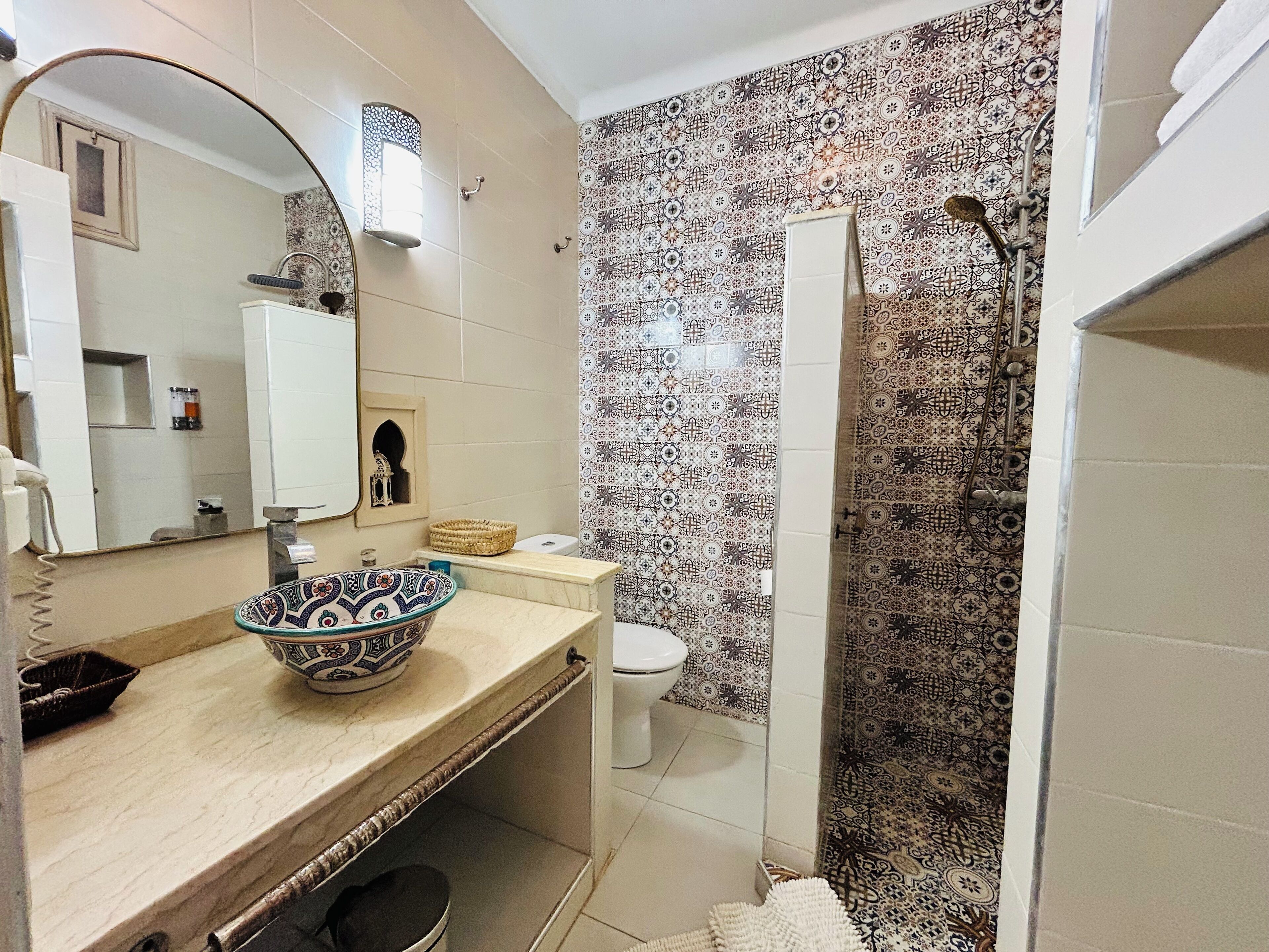 A bathroom with a patterned tile wall, a sink with a decorative bowl, a toilet, and a shower with a curtain.