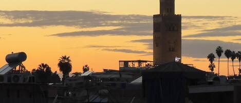 A cityscape at sunset with a prominent tower and palm trees.