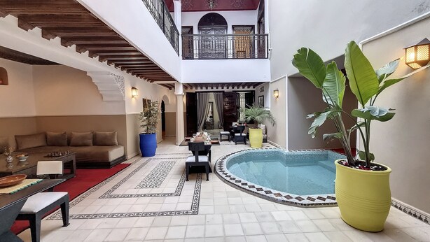 Une cour avec une piscine, des espaces aménagés pour se détendre et une table à manger.