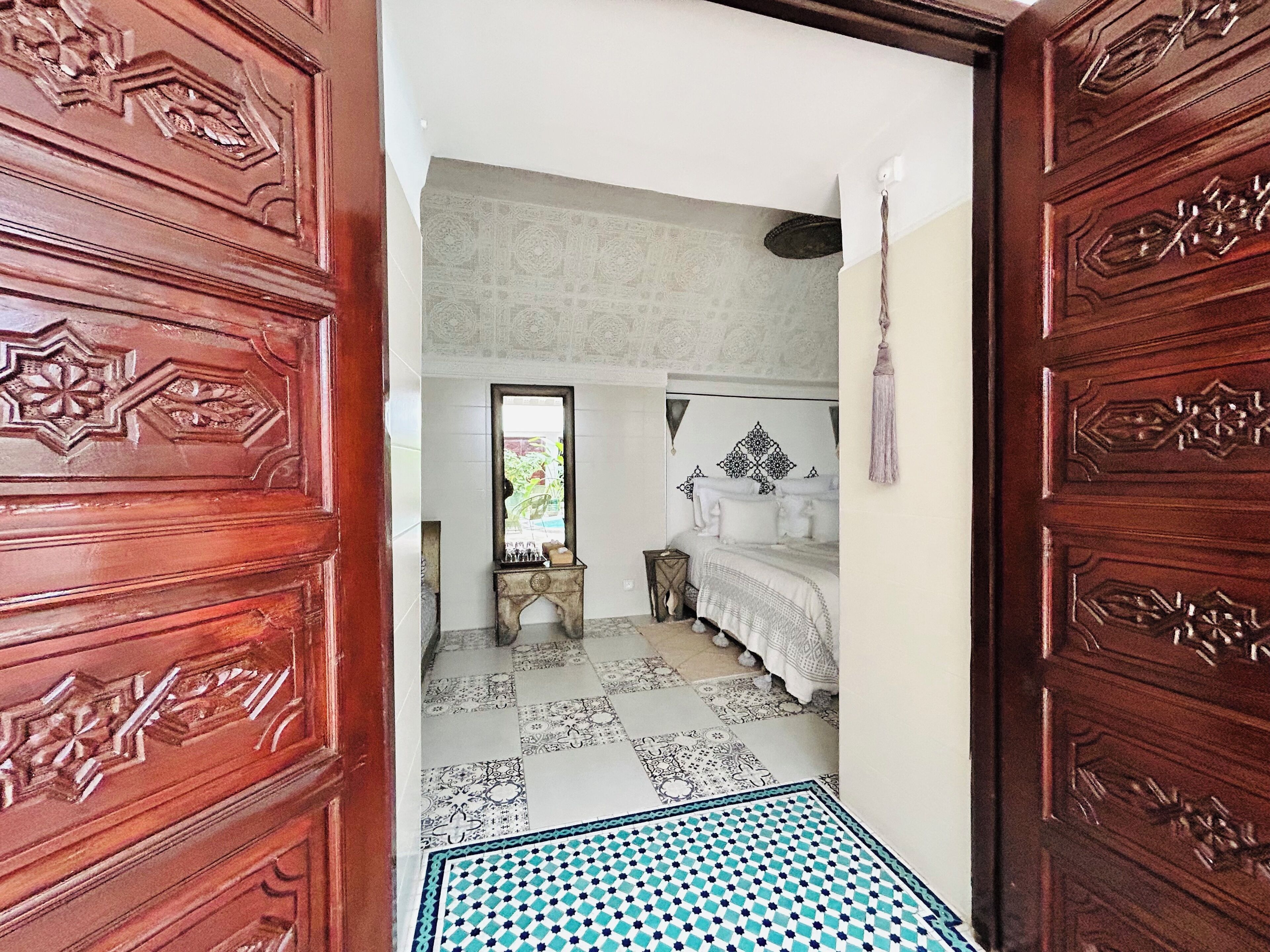 Une pièce avec un sol à motifs, un lit avec une literie blanche, un miroir et un mur décoratif.