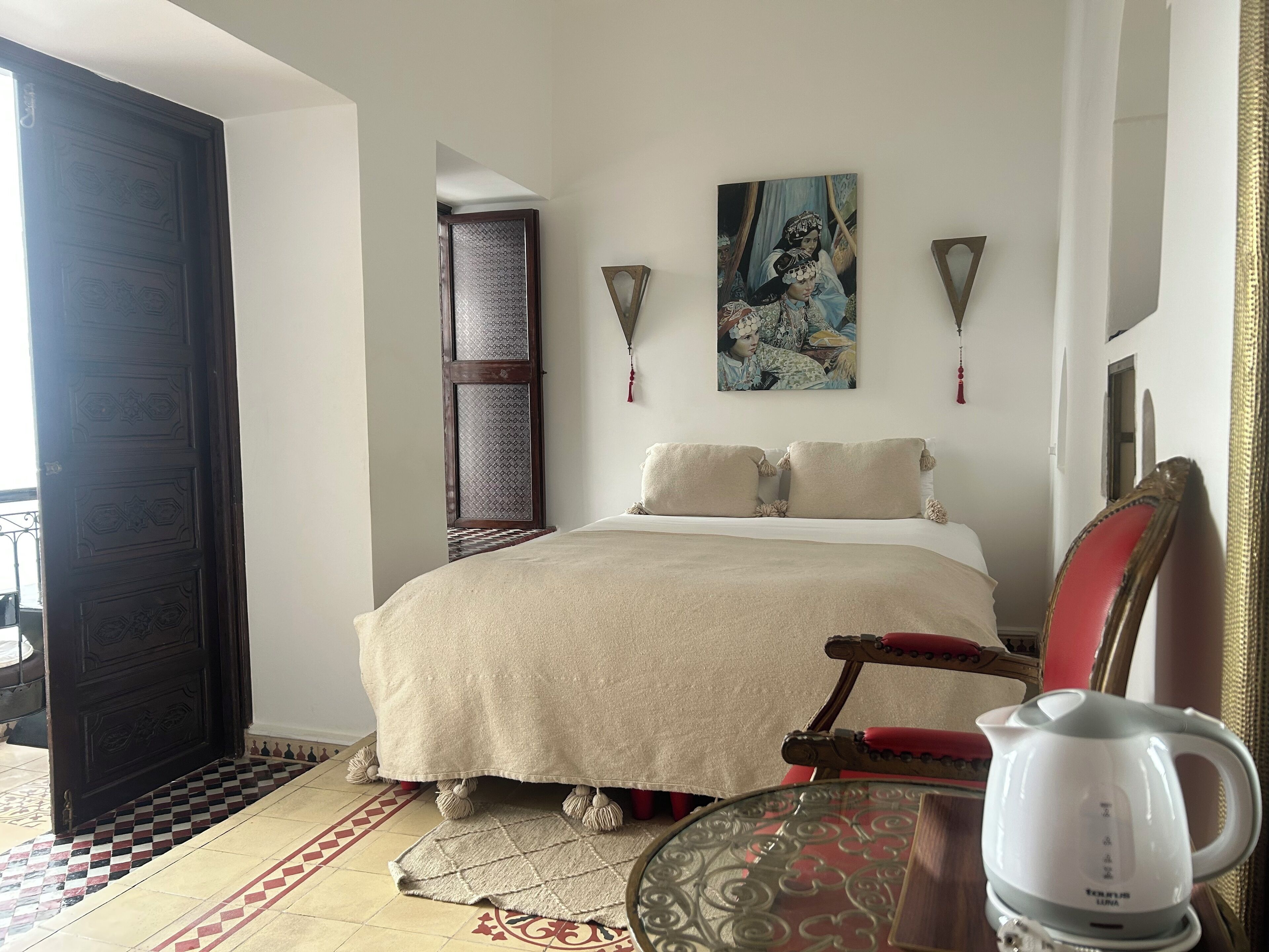 Una habitación de hotel con una cama, una silla, una mesa y una tetera.