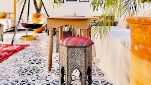 Une terrasse ensoleillée avec un sol à motifs, une balançoire suspendue et une table entourée de chaises.
