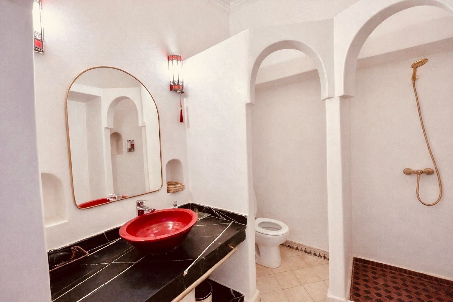 A bathroom with a red sink, a white toilet, a shower, and a large mirror.