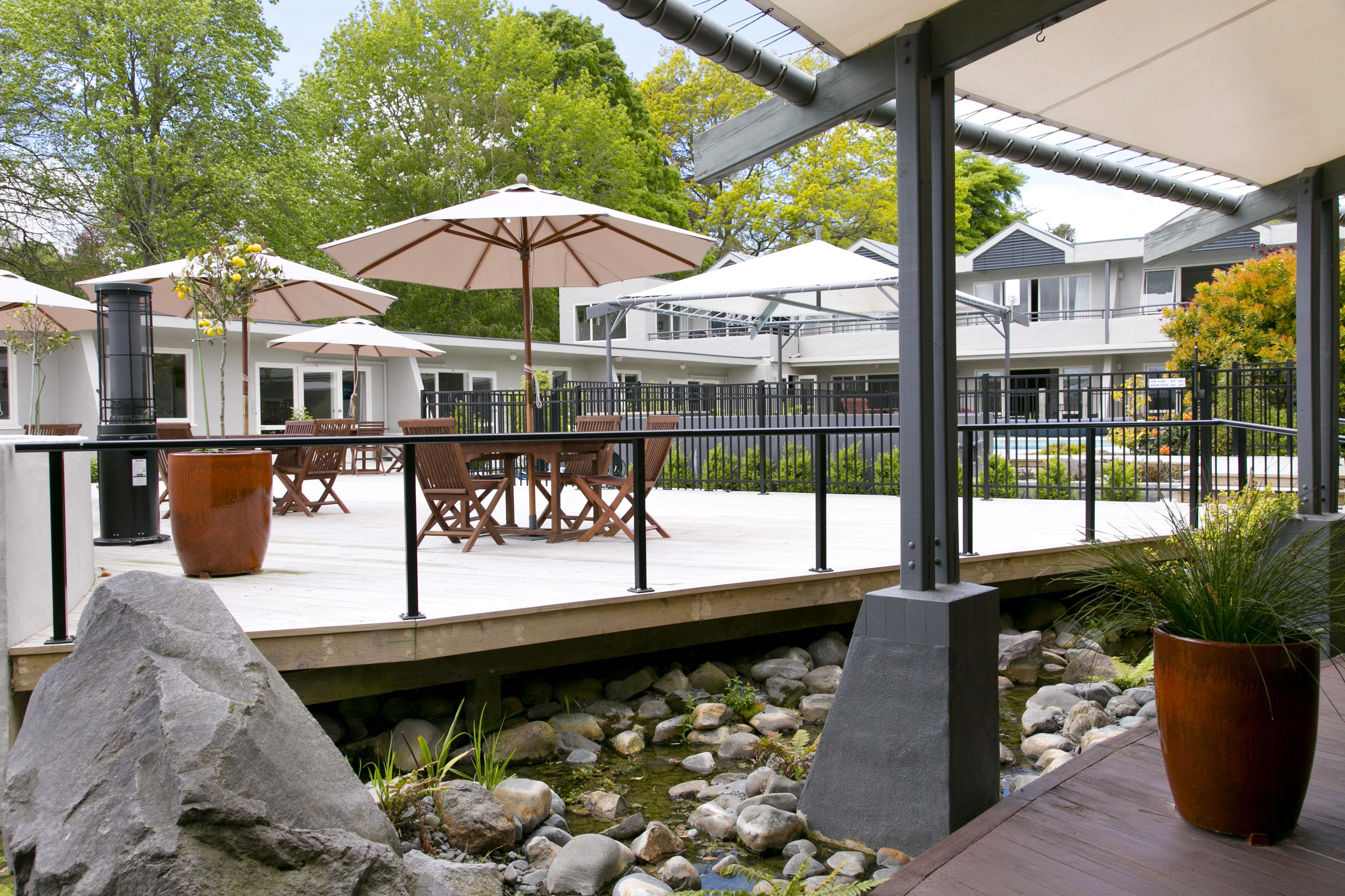 A covered outdoor patio with tables and chairs, umbrellas, and a stone pathway leading to a building.