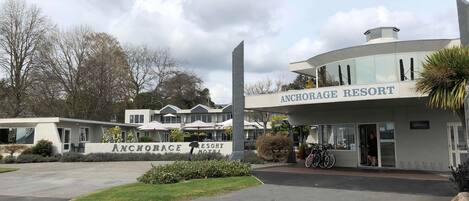 The exterior of Anchorage Resort, featuring a modern building with a prominent sign, a covered outdoor seating area, and a parking lot.