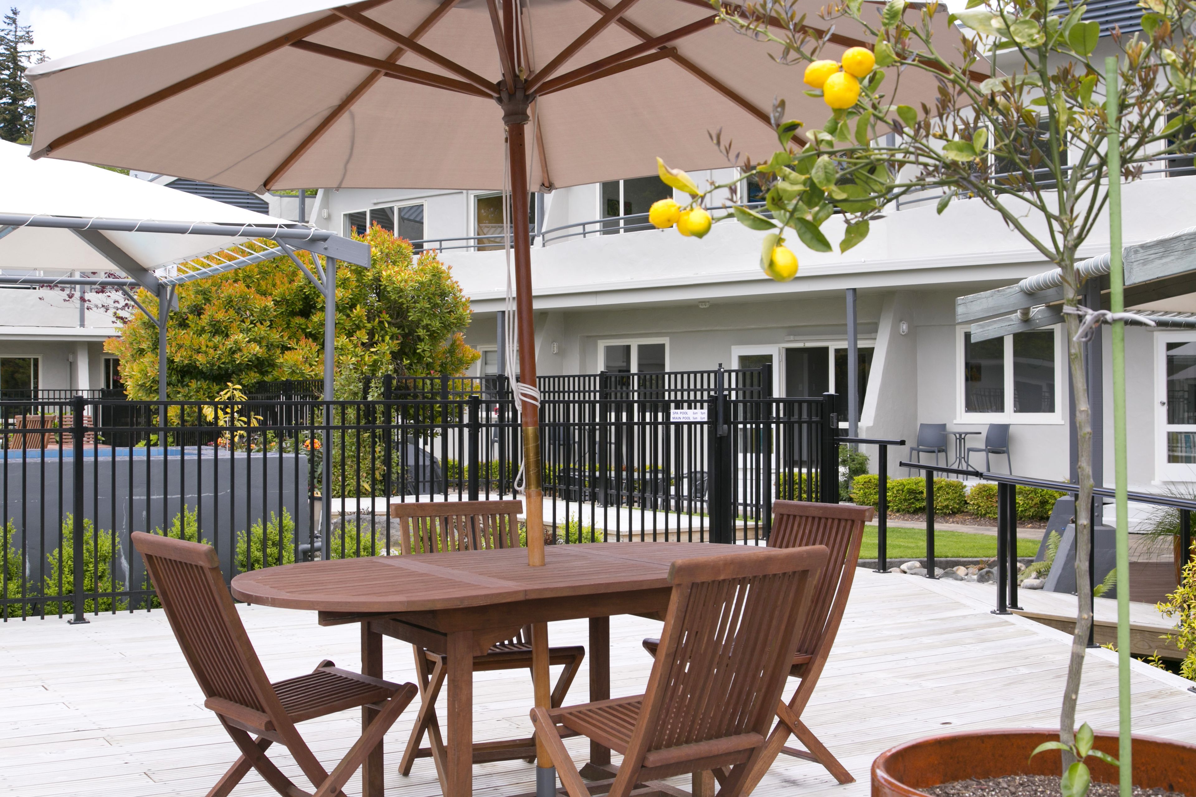 A wooden deck with a table and chairs, a large umbrella, and a potted plant with yellow flowers.