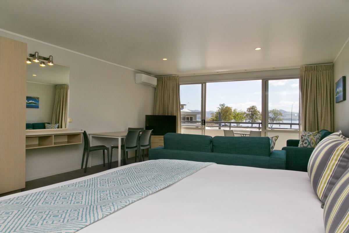 Une chambre d’hôtel avec un grand lit, un bureau, un canapé vert et une vue sur l’extérieur.