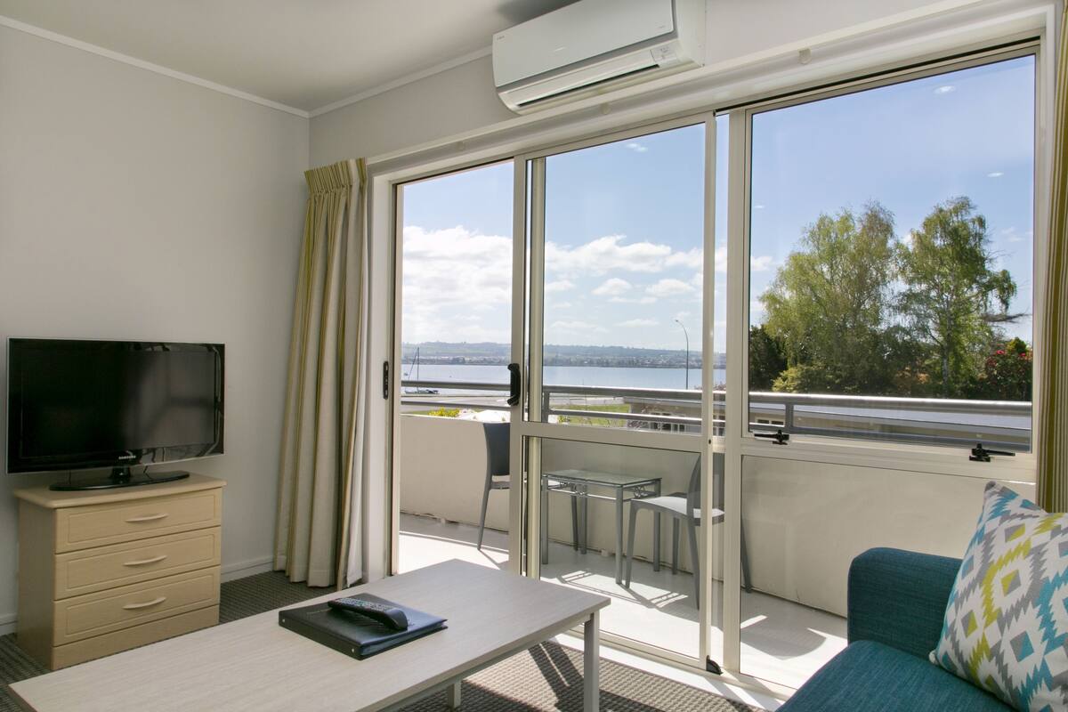 Une chambre d’hôtel équipée d’une télévision, d’un bureau, d’un canapé et de grandes fenêtres donnant sur l’extérieur.