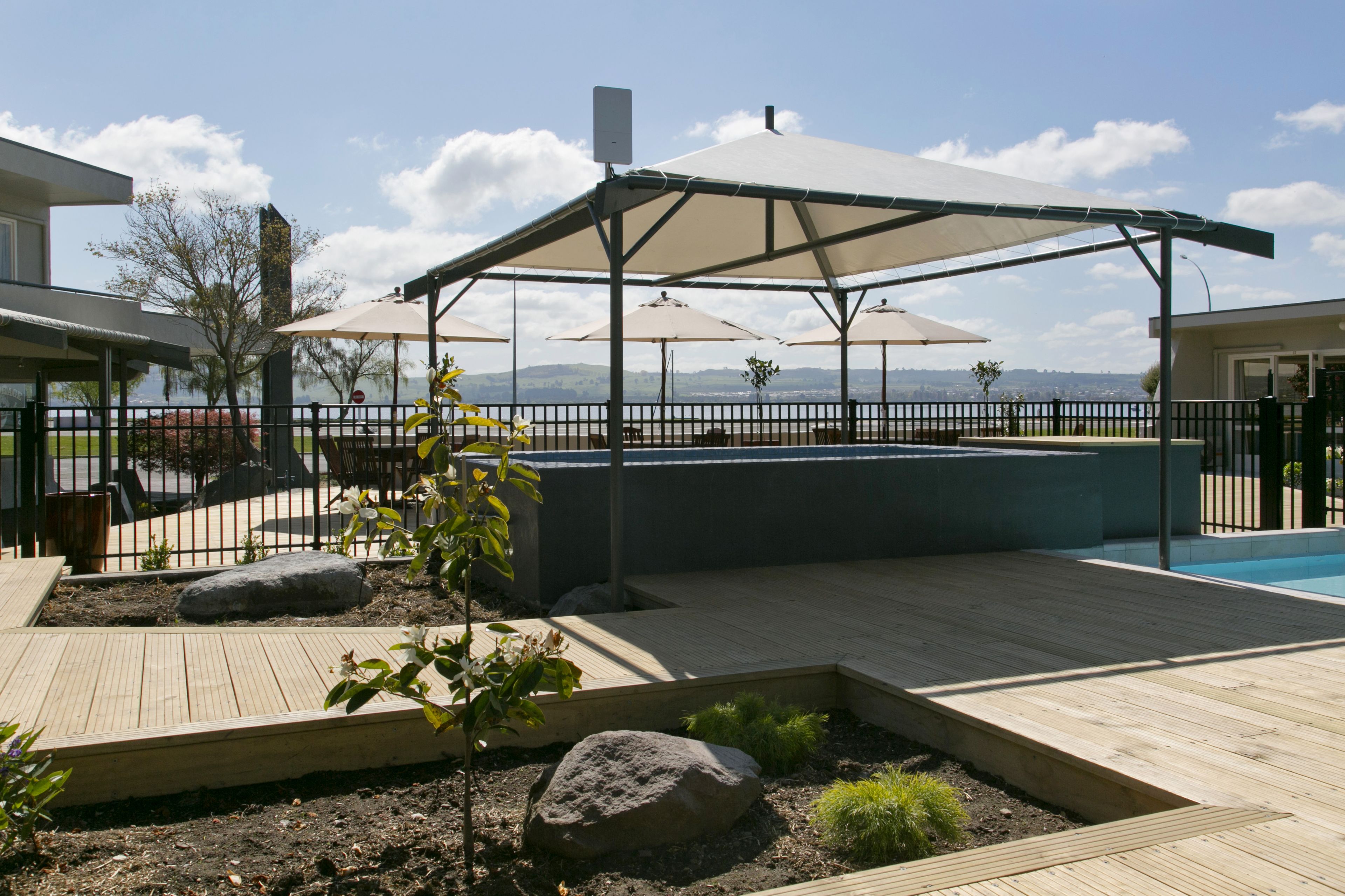 Una terraza de madera con piscina, sombrillas y vistas a las montañas.