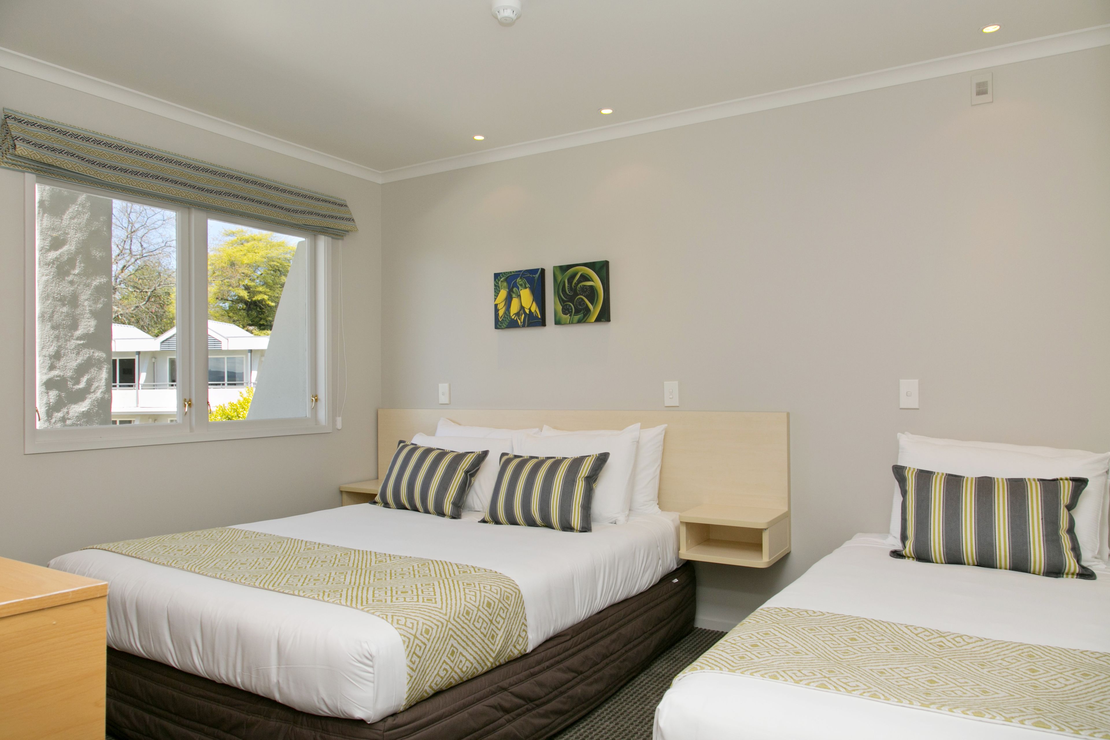 Habitación de hotel con dos camas, una ventana que da a casas y dos obras de arte colgadas en la pared.