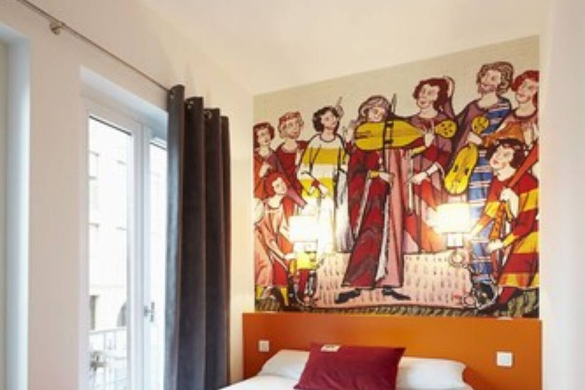 A hotel room with a bed, a large wall mural, a window with curtains, and a view of the outside.
