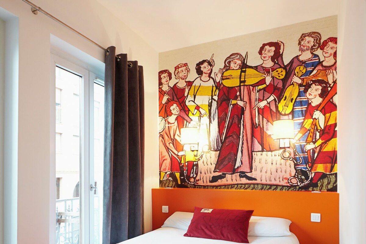 Una habitación de hotel con una cama grande, un mural en la pared y una ventana con cortinas.