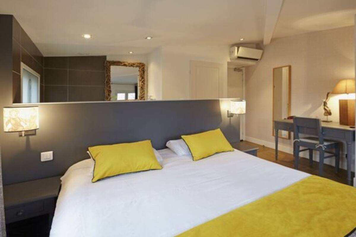 A hotel room with a bed, two bedside lamps, a desk with a chair, and a large mirror.