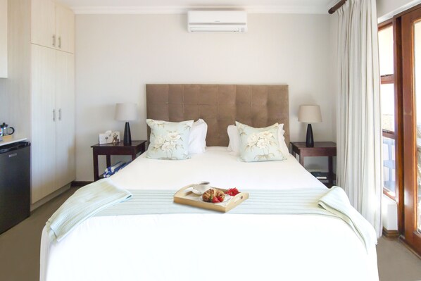 Habitación de hotel con una cama grande, dos mesitas de noche, un pequeño rincón con fregadero y una ventana con cortinas.