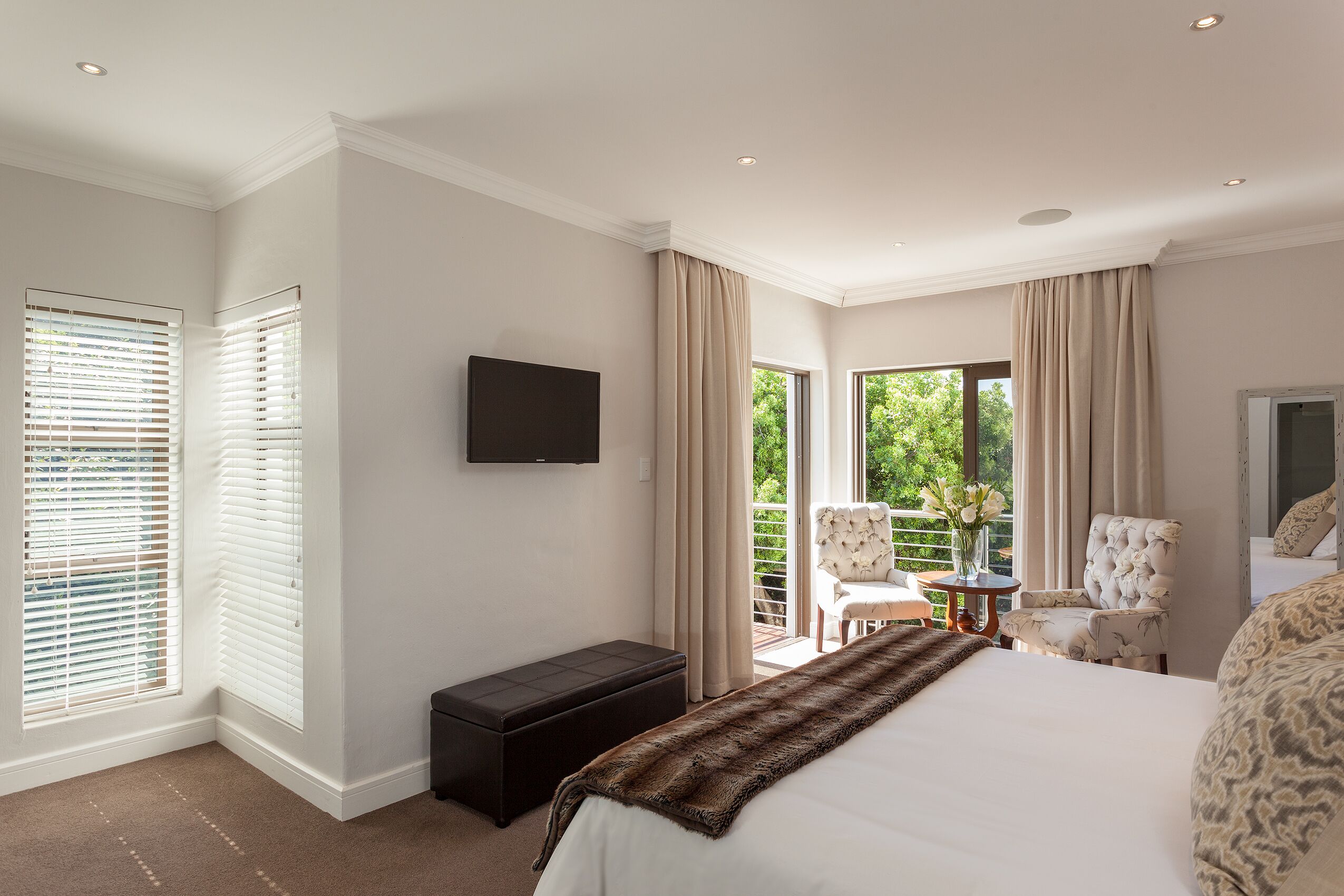Quarto com uma cama grande, televisão de tela plana, um banco e uma cadeira perto de uma porta de vidro deslizante que dá para uma varanda.
