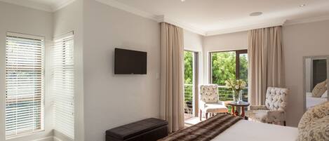 A bedroom with a large bed, a flat-screen TV, a bench, and a chair by a sliding glass door leading to a balcony.