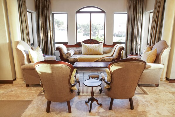 A living room with a sofa, two armchairs, a coffee table, and a small table with a cup and saucer.