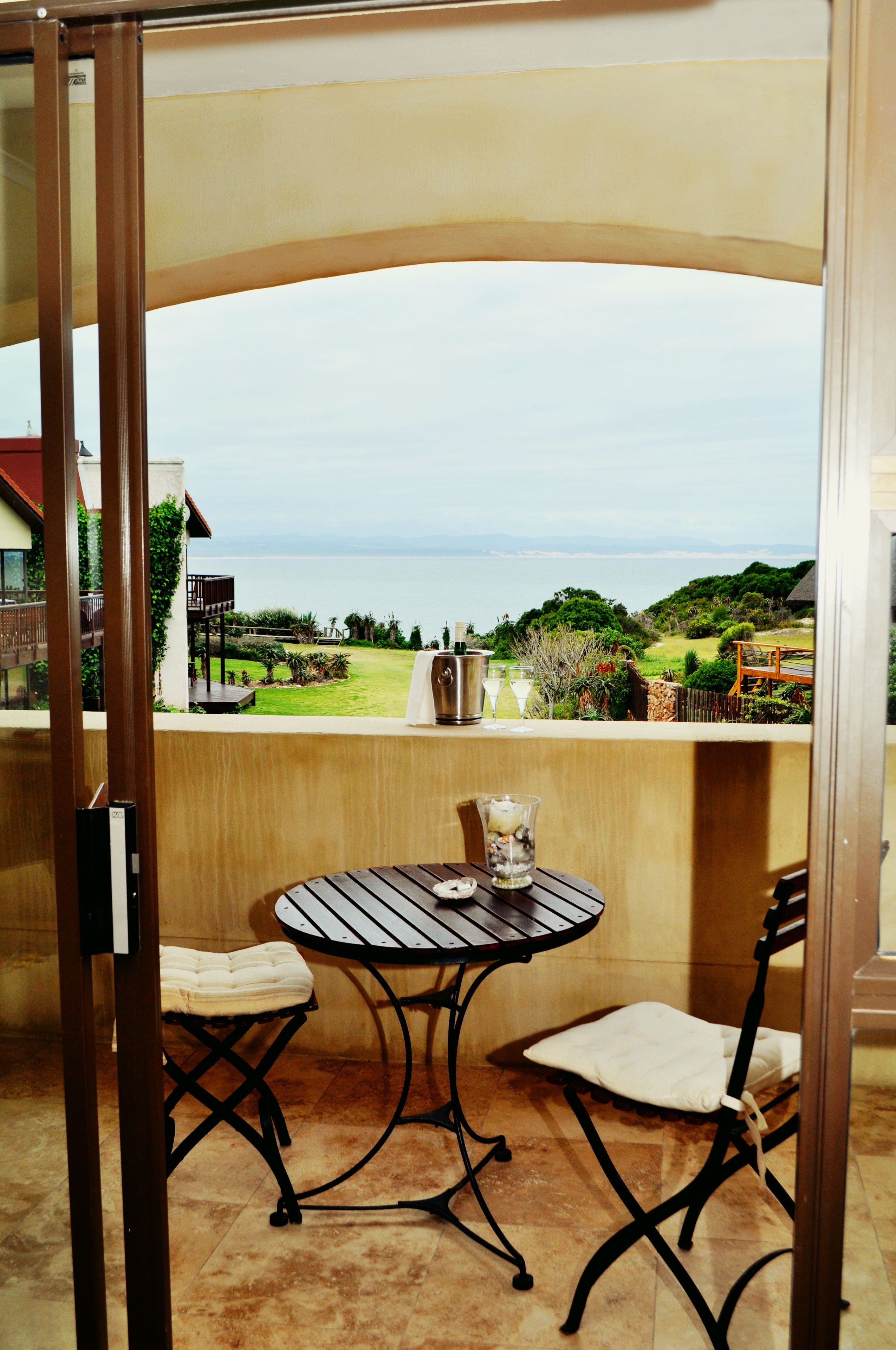A balcony with a table and chairs, overlooking a grassy area and the sea.
